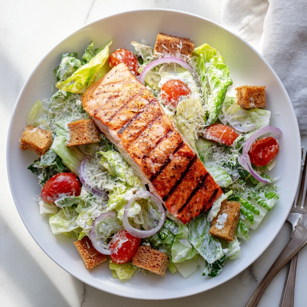 Golden brown salmon fillets atop a bed of romaine with tangy homemade Caesar dressing and shaved Parmesan cheese