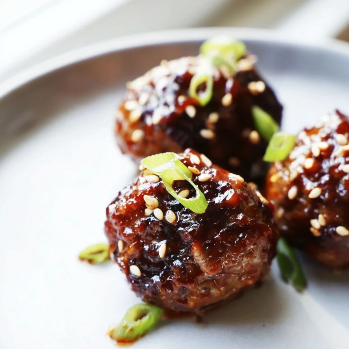 Golden brown Korean BBQ meatballs topped with sesame seeds and green onions on a white platter