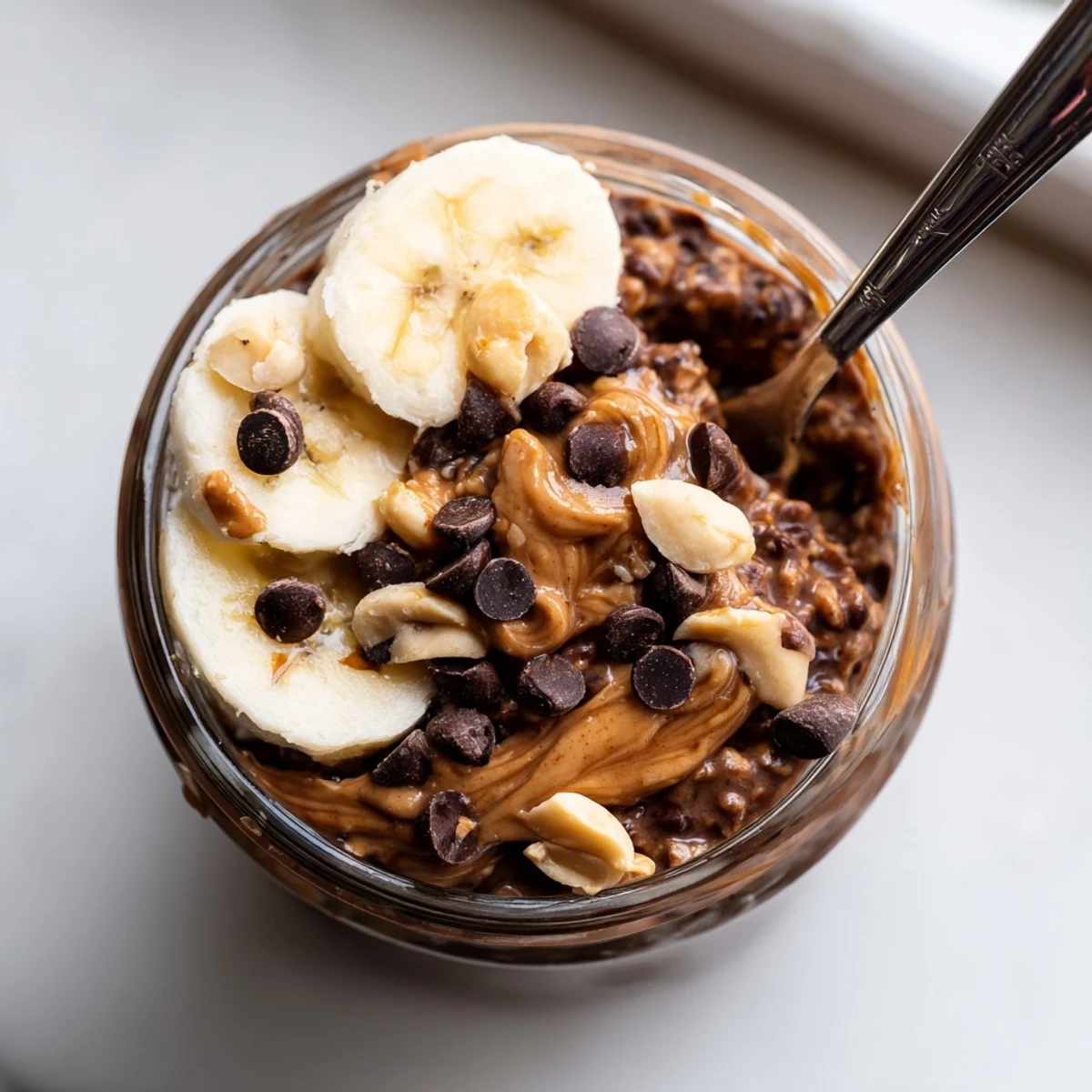 Thick chocolate peanut butter overnight oats served in mason jar with banana slices