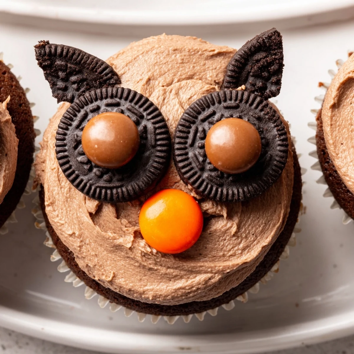 Chocolate Oreo owl cupcakes topped with twisted cookie eyes and bright orange candy beaks