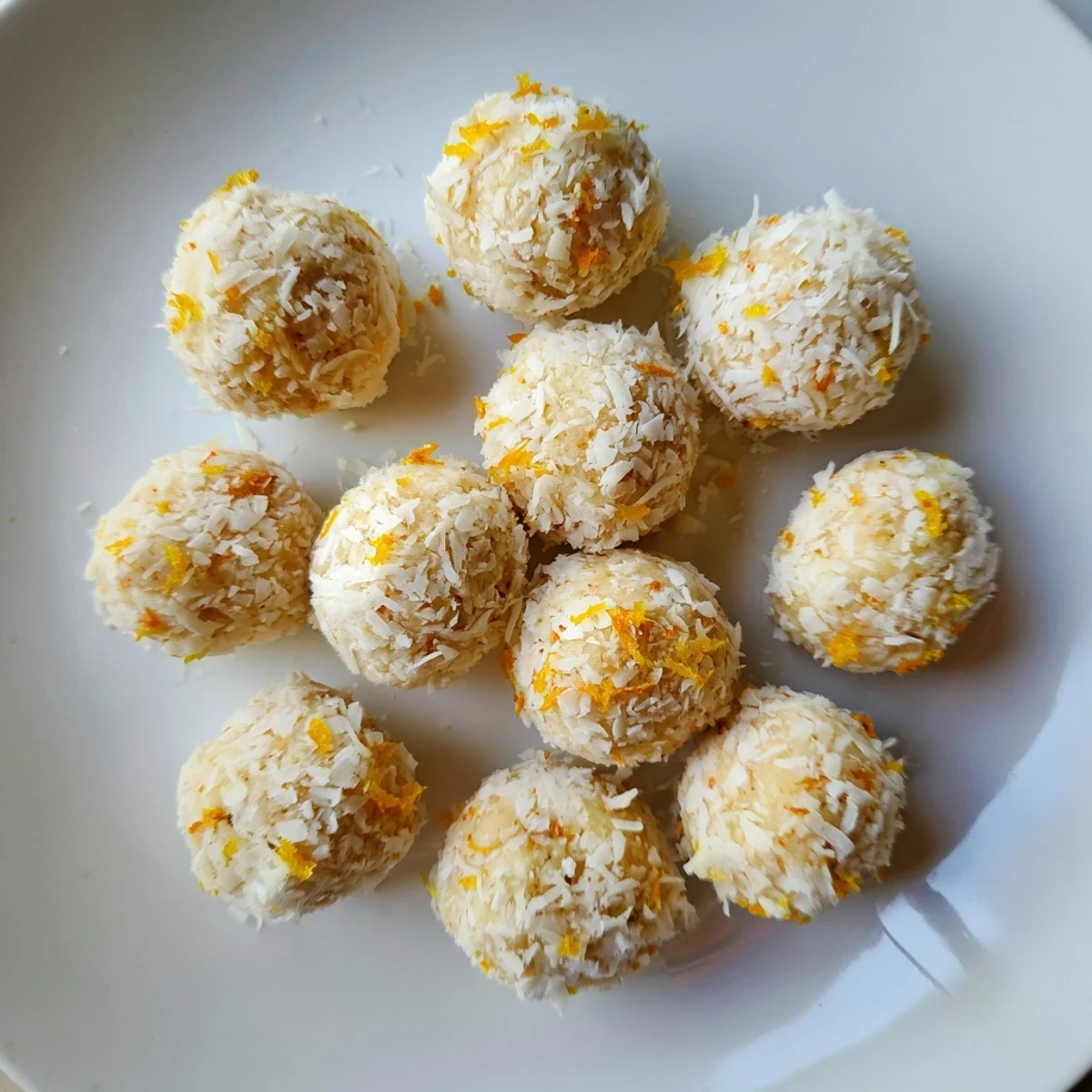 Fresh no-bake Citrus Bliss Bites rolled in coconut on a white serving platter
