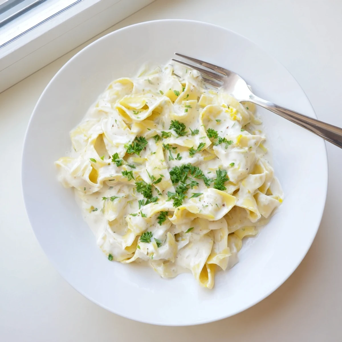 Golden wide egg noodles coated in rich creamy Parmesan sauce served in white bowl.