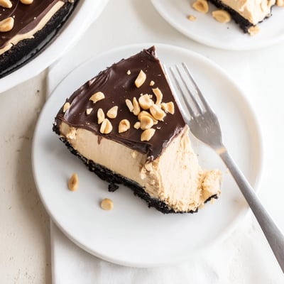 Silky no bake peanut butter pie topped with glossy chocolate ganache and chopped peanuts